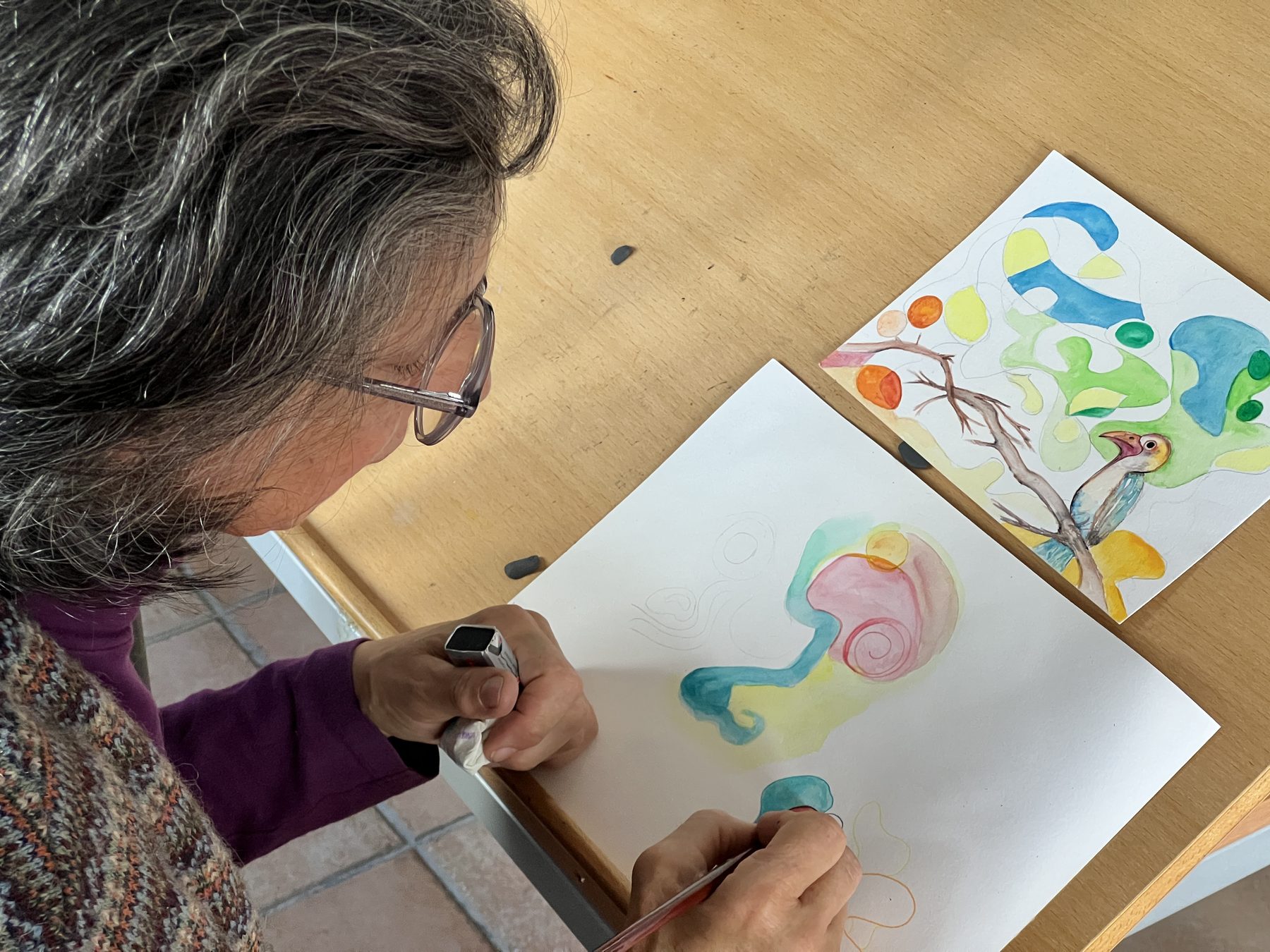 Ana Soares a desenhar, vista de cima, com uma aguarela de cores vivas ao lado